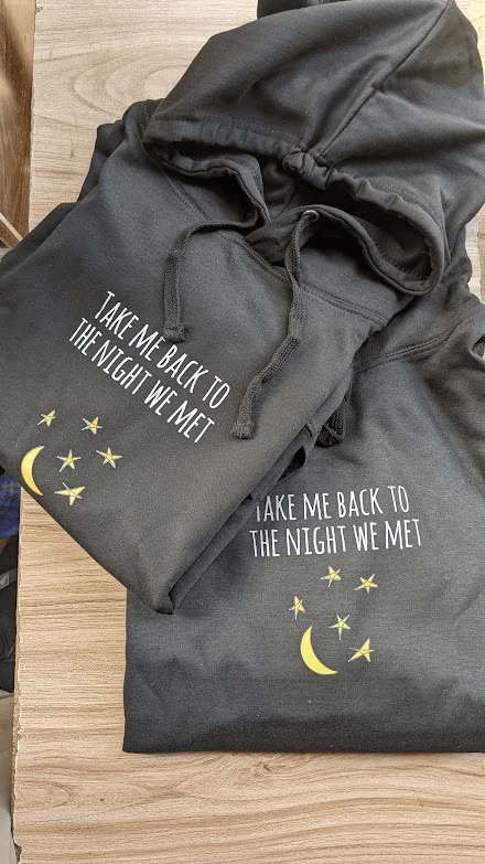 Matching pair of black hoodies with Take Me Back to the Night We Met typography and moon graphics